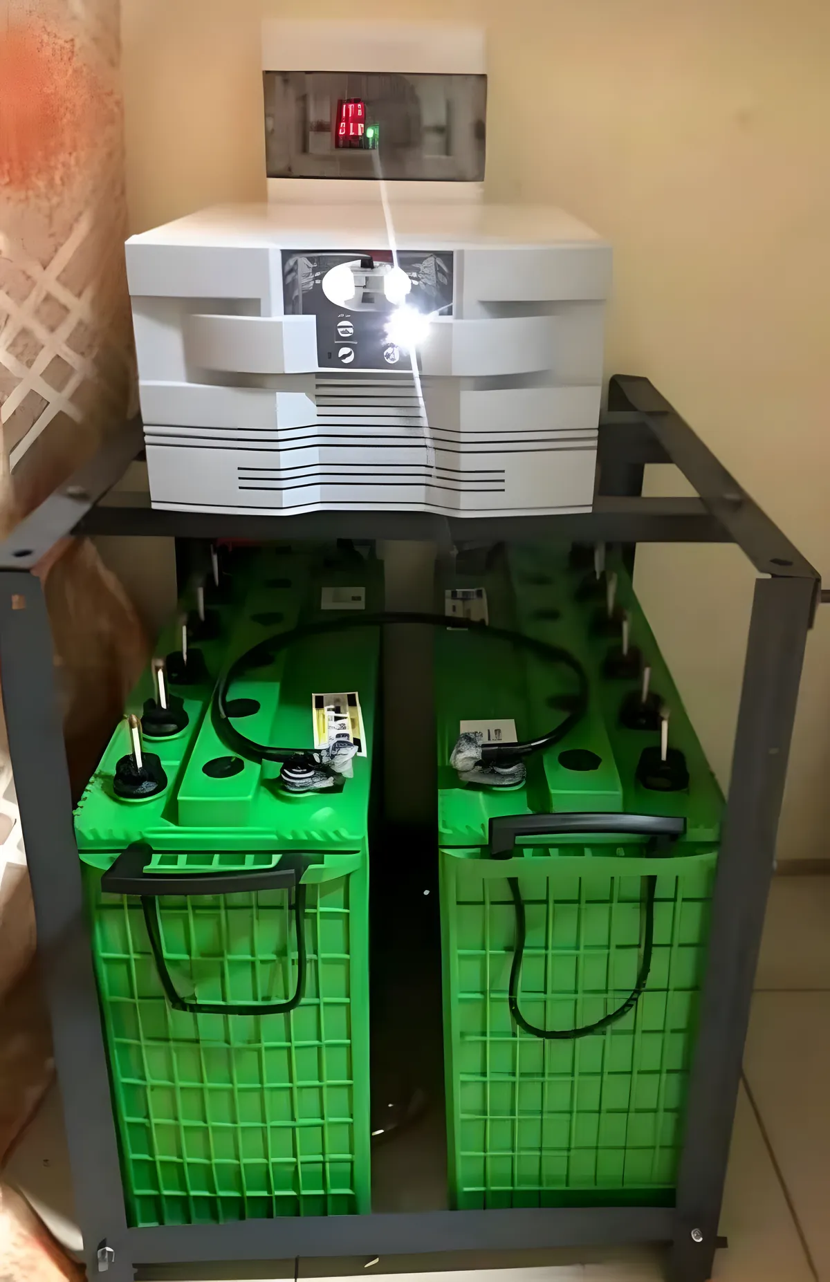An inverter on a steel stand above two green tubular batteries